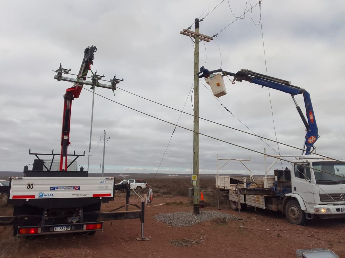 Dos camiones con hidrogrúa trabajando sobre una línea eléctrica, uno con canasta para personal